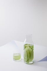 high angle view of bottle and glass with water and sliced cucumbers on white paper surface isolated on grey