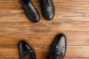 Top view of mens and childrens black classic shoes on wooden background, fathers day concept