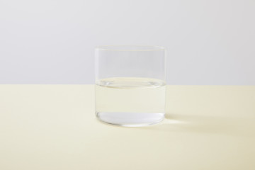 Glass with water on yellow surface isolated on grey
