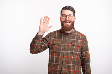 Young bearded man smiling at the camera is showing hello gesture presenting himself to the world on white background. © Vulp