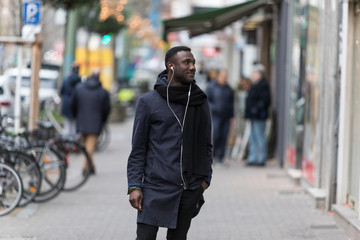 Black Man Standing on Sidewalk Listening to Earphones with Head Turned