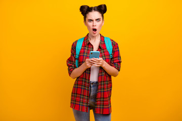 Photo of beautiful shocked student lady hold telephone read email exam bad results walk college open mouth wear blue bag casual plaid shirt jeans isolated yellow color background
