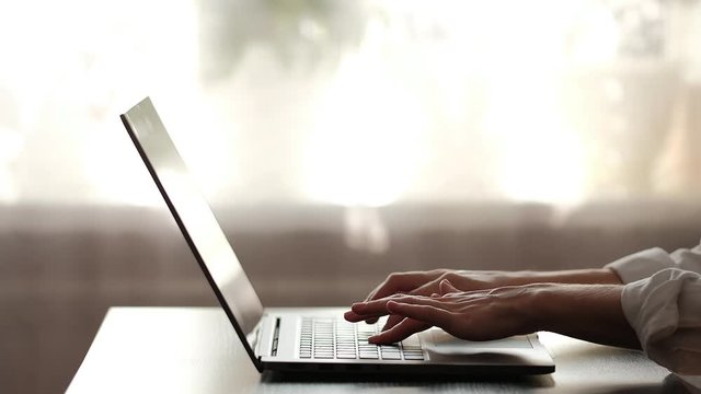 Close up plan of opening laptop and typing. Silhouette and low key shot. Working at home and freelance concept. Typing hads in low key on a window background.