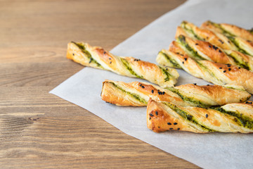 salty sticks of puff pastry sprinkled with cumin and greenery on a wooden background