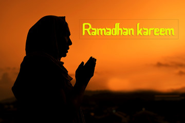 Silhouette of Female Muslim praying in during sunset time with "RAMADHAN KAREEM" wording for islamic concept.
