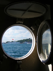 Fototapeta na wymiar View from the ship’s cabin through a round porthole, on a green sea island. Sea transport concept. Transportation of people by sea