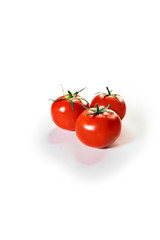 Three red tomatoes stand on a white background. Tomatoes stand nearby and form a triangle. The background is in defocus. Bright color, isolated objects.