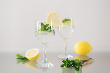 Two glasses of mineral water with lemon and fresh mint on glass surface. Sparkling drink with citrus and herbs