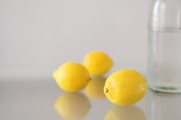 Three  whole lemons and bottle of mineral water on glass table. Citrus fruit. Lemonade ingredient