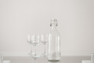 Empty glass bottle and three empty wine glasses on transparent table. Glassware concept