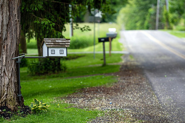 a traditional American wooden mailbox that looks like a cottage, on the side of a village road