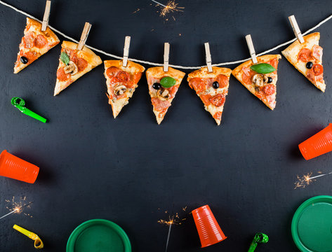 Slices of pizza in the form of a garland with the attributes of a party and Bengal Candles. Pizza slices on a gray concrete background. Space for text. Pizza menu. Birthday with fast food. 