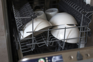 Large white bowls in the compartment of an open dishwasher
