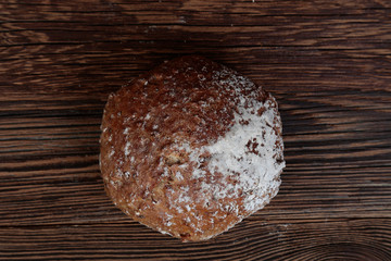 Top view of a fresh, dark, hexagonal bread sprinkled with flour. Loaf on a rustic, wooden table with brown boards.