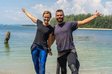 Funny couple at the seashore in wetsuits.