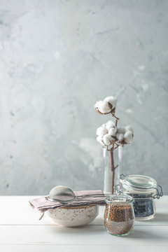 Coffee beans and instant coffee in glass jars, cotton flowers and kitchenware on white wooden table with grey concrete wall at background. Details of still life in the home interior. Cosy concept.