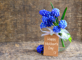 Happy Mother's Day greeting card with blue springMuscari flowers in a glass vase and tag with text..Selective focus.