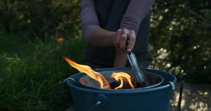 Young woman turning coals on barbebcue with flames