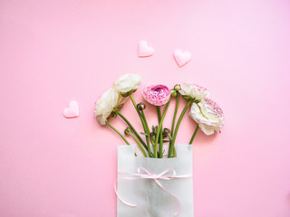 Pinke und weiße Ranunkeln in einer weißen Papiertüte mit Schleife auf einem rosa Hintergrund, Geburtstag, Geschenk, Liebe