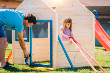 Dad building assembling wooden playhouse with daughter at home in the backyard garden