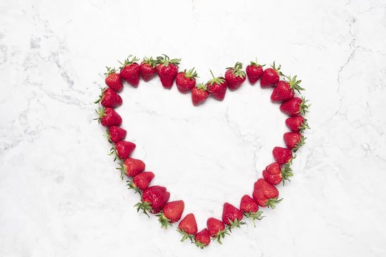 top view stop motion movie, little strawberries compose an heart on a white marble table
