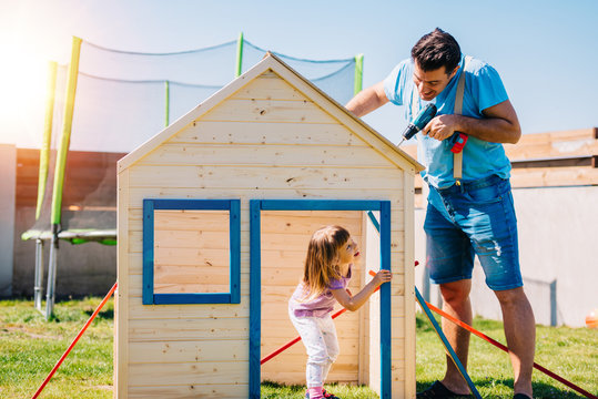 Dad building assembling wooden playhouse with daughter at home in the backyard garden