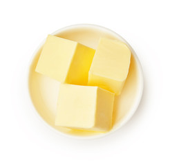 Butter pieces in white bowl isolated on white background. Butter cubes. Top view.