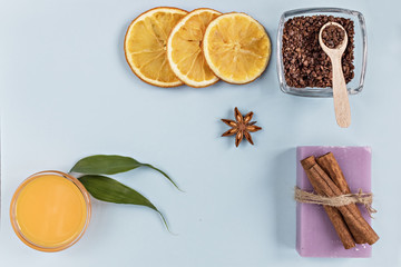 Obraz na płótnie Canvas On a blue background are care products: lavender soap and mango cream for face and body after, coffee scrub. For aromatherapy: cinnamon sticks, anise star, sliced orange circles. Spa concept.