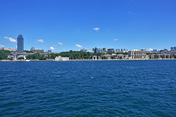 Panorama of Istanbul from the Bosphorus Strait. Seagulls fly over the blue water. Visible are modern high-rise buildings and an old historic palace. Clouds in the blue sky.