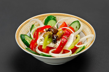Ceramic bowl with fresh cucumber, tomato, onion, paprika, feta and marinated olives salad on grey background