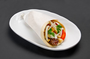 Meat, French fries and vegetables wrapped in pita with sauce on white ceramic plate on grey background