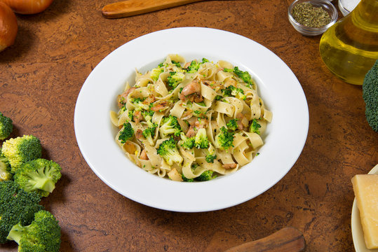 Authentic Italian fettuccine pasta dish with chicken breast and broccoli on a brown table. 