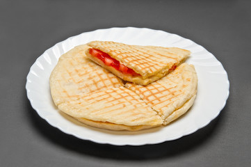 White ceramic plate with vegetarian pita with tomatoes and cheese on grey background