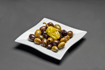 White ceramic plate with marinated olives, pepper and spice salad on grey background
