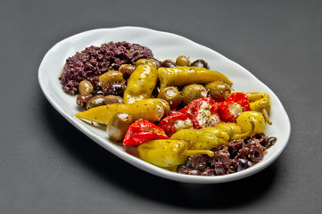 White ceramic plate with marinated olives, stuffed with feta pepper and spice mix on grey background