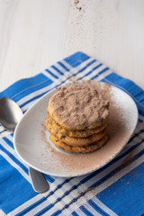 Aerial view of plate with chocolate chip cookies, with falling chocolate powder and spoon on blue napkin and white table, vertical