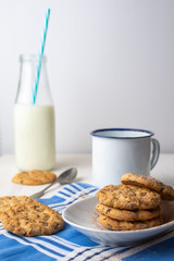 Close-up of white plate with chocolate chip cookies, cup, spoon and bottle of milk with blue straw, on blue napkin and white background, vertical