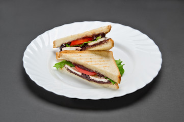 White ceramic plate with two sandwiches with feta, tomato, lettuce and olive pate on grey background