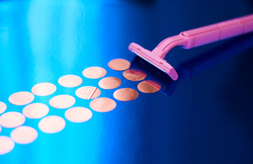 Blue glossy background and female pink razor for depilation with round confetti.