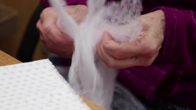Elderly seamstress selecting filter padding for handmade production of covid virus mask