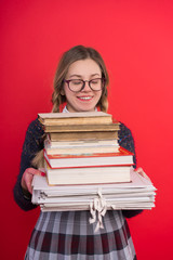 Schoolgirl teenager with pigtails and glasses, in a checkered skirt, on a red background and holds a bunch of books, vertical