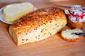 Loaf of bread with seeds, butter, jam in bottle on table.