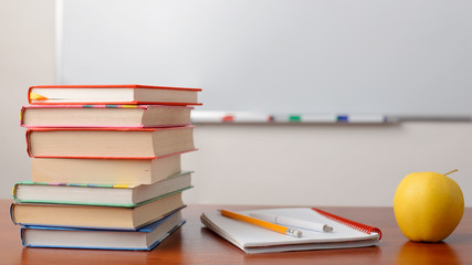Picture of stack of books on the table against whiteboard in the classroom
