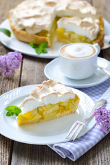 Leckerer Rhabarberkuchen mit Baiserhaube und Cappuccino auf einem Holztisch mit frühlingshafter...