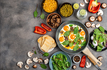 Homemade fried eggs in a pan with ingredients on a gray background. Healthy breakfast. Top view with space for text.