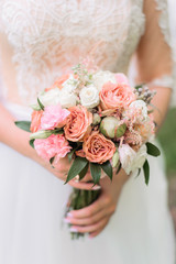 The bride holds a wedding bouquet of peach and white roses and flowers. 