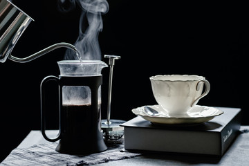 The steam from a pot  to a French press coffee maker on the old wood table and black background with a book,notebook,pencil, Warm drinks make good healthy, Selective focus, Mono vintage style.