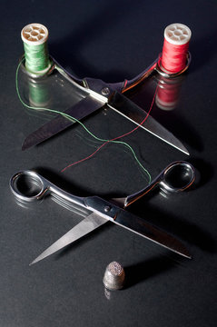 fotografia de 2 tijeras abiertas con un dedal y 2 bobinas de hilo rojo y  verde