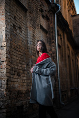 Girl in a red blouse and a gray cardigan on the background of the old brick wall