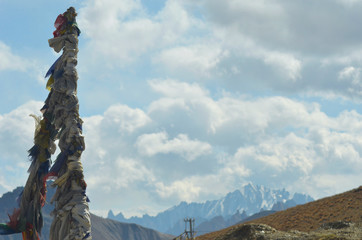 Obraz premium Hundreds of prayer flags have been wrapped around a pole. The Ladakh Mountains are in the background, part of the Trans-Himalayan Range. The sky is blue with white clouds.